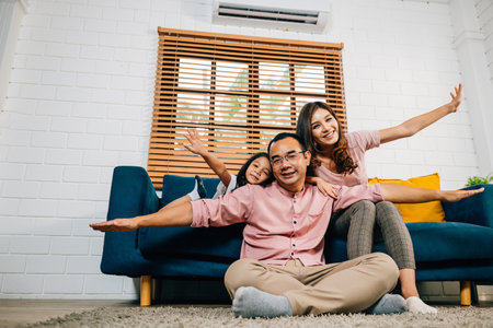 An interracial family shares a moment of joy and togetherness at home. Playing plane games, a father with his daughter on his shoulders and a smiling mother showcase the essence of a supportive family.の写真素材