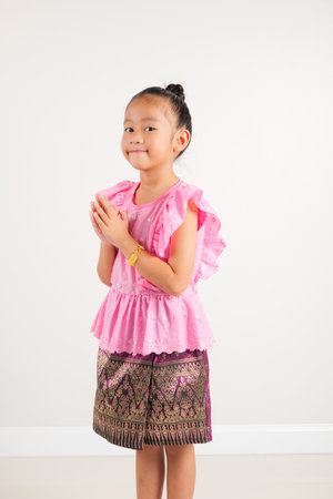 Portrait of Thailand kid girl smiling traditional Thai dress costume posing to pay respect in studio shot isolated white background, Happy kindergarten child sawasdee symbol or welcomeの写真素材