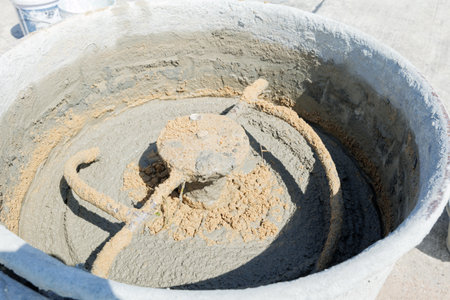 Mixer blades visible churning gray mortar and sand inside, highlighting the concrete preparation process for building projects.の写真素材