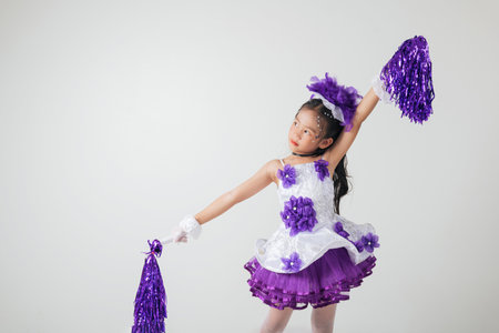 Young girl dressed in cheerleading gear, purple pom-poms in hand. Studio photo with white background, full of festive energy. cheerleader kidの写真素材