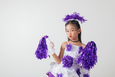 Smiling cheerleader girl wearing purple and white outfit with pom-poms. Studio portrait exuding energy and joy against a white background. cheerleader kidの写真素材