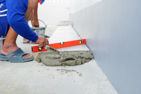 A worker smooths a layer of gray mortar, creating an even foundation for securely setting floor tiles in place.の写真素材