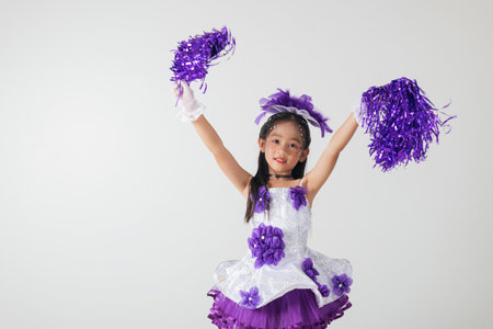 Adorable kid in cheerleading outfit with purple pom-poms. Studio photo on white, showcasing her happiness and energetic cheer. cheerleader kidの写真素材