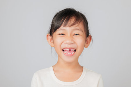 Tooth loss lesson by dentist for happy Asian girl, smiling with missing tooth. Kid shows gap, learning dental care and growing healthy new teeth after loss. isolated white backgroundの写真素材