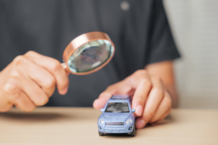 Magnifying glass focused on a car model, representing the search for automobile repair or insurance options. Concept of vehicle assessment and ensuring maintenance with careful inspection.の写真素材