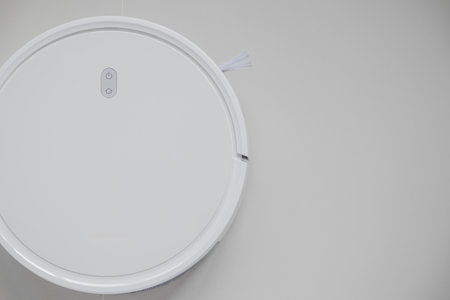 White automatic floor cleaner with side brush on tile flooring. Top view of robot vacuum cleaner removing dust, showcasing modern smart home cleaning technology for spotless and efficient maintenanceの写真素材