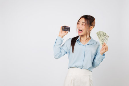 Woman excited and happy while holding credit card and dollar money fan, payment money shown clearly as symbol of freedom and personal control over her spending habits. isolated studio white backgroundの写真素材