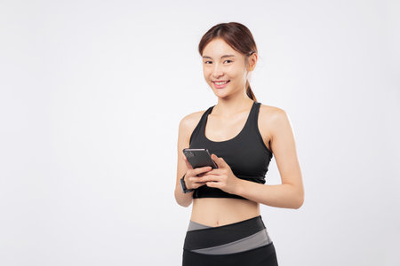 Holding a phone while using another phone gesture, this sporty woman balances her fitness lifestyle and tech habits in one confident gym-ready portrait. isolated studio white backgroundの写真素材