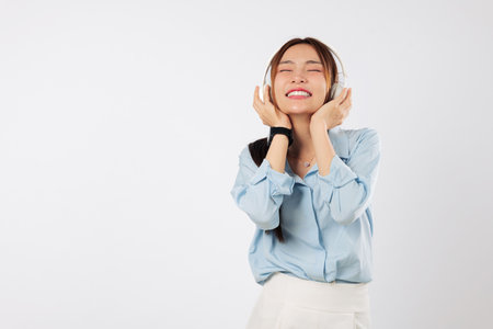 Listening music with a soft smile, young Asian woman closes her eyes and enjoys peaceful emotions, lifestyle bliss, and the rhythm of beautiful music. isolated studio white backgroundの写真素材