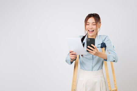 Holding phone and bill paper, woman on crutches smiles after accident. She feels confident despite accident, managing recovery and payment tasks with ease. insurance isolated studio white backgroundの写真素材