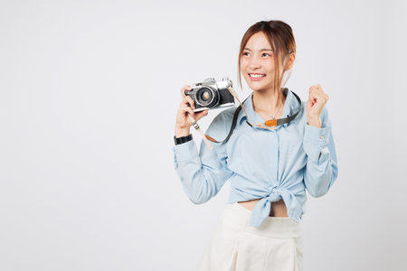 Tourist holding vintage camera smiles wide, cheerful tourist moment. Portrait happy Asian woman shows positive travel energy during her journey. Excited summer isolated studio white backgroundの写真素材