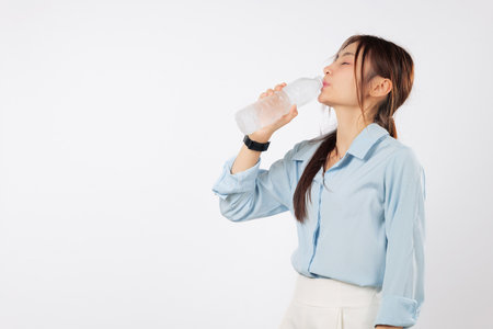 Young asian woman holds plastic water bottle, eyes closed, enjoys a refreshing drink because she wants to drink some water and stay hydrated, isolated studio white backgroundの写真素材