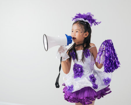 Young girl in a purple and white cheerleader costume poses with a megaphone. Studio image on white, capturing her enthusiasm and festive vibe.の写真素材