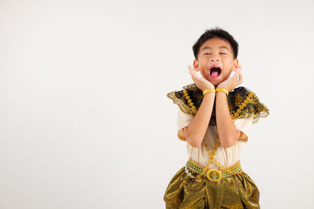 Portrait Thailand kid boy smiling traditional Thai dress costume raises her fists in celebration of her success, studio isolated white background, primary child saying yes with excitement winningの写真素材