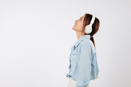 Side view of young Asian woman listening music with headphones and smiling, eyes closed with happiness, expressing peaceful emotions brought by calming music. isolated studio white backgroundの写真素材