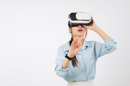 Asian woman with vr headset glasses explores virtual reality, hand touching future game application, happy with vr experience, a businesswoman interacting on a white screen, isolated white backgroundの写真素材
