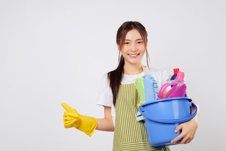 Cleaning expert smile woman in gloves shows thumbs up, holding a bucket with cleaning products. Positive happy cleaning service presentation. isolated studio white backgroundの写真素材