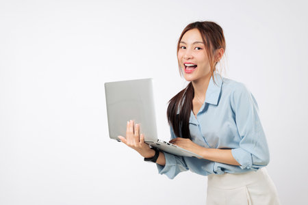 Happy Asian Young woman using laptop computer smiling while working, excited typing and focused on business task with her second laptop nearby. isolated studio white backgroundの写真素材