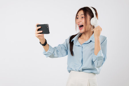 Win emotion lights up her face excited as woman wear headphones plays game, raises hand to celebrate and later laughs with joy after the next mobile win.watch video online isolated white backgroundの写真素材