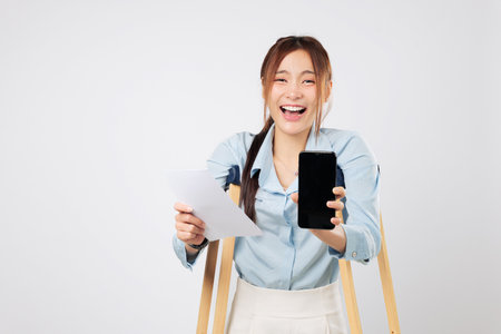 Patient on crutches holds bill paper and phone with blank screen proudly. Crutches symbolize support as she navigates accident payment confidently. insurance isolated studio white backgroundの写真素材