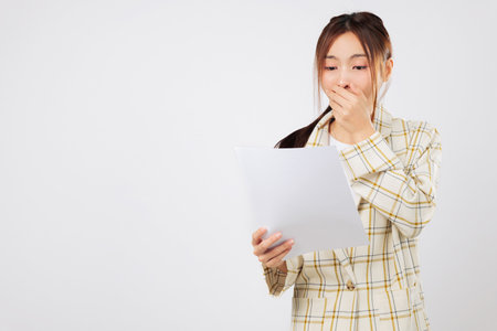 Shocked and stressed, Asian woman stares at bills piling up, her financial situation worsening as she battles financial problems alone. isolated studio white backgroundの写真素材