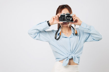 Camera focused Asian young woman enjoying her trip, taking clicking with camera. Happy Cheerful female traveler tourist captures fun travel moments in style. isolated studio white backgroundの写真素材