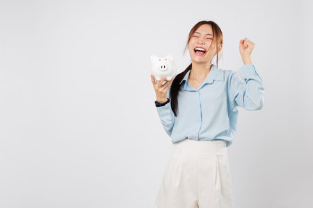 Happy woman smiling excited with a fist up holding piggy bank and piggy save money to win financial goals, success savings in smart budget and invest plans. isolated studio white backgroundの写真素材