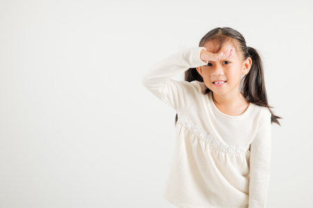 Searching concept. Asian young girl kid looking far away with hand over head at studio shot isolated on white background, Portrait of Happy kindergarten child looking at distance with eyes shadedの写真素材
