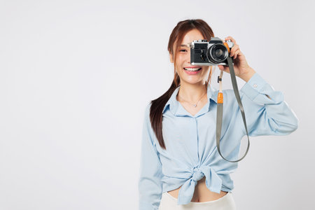 Camera carrying traveler taking shots with her images camera. Happy smiling Asian young woman enjoying photography adventure on summer holiday. isolated studio white backgroundの写真素材