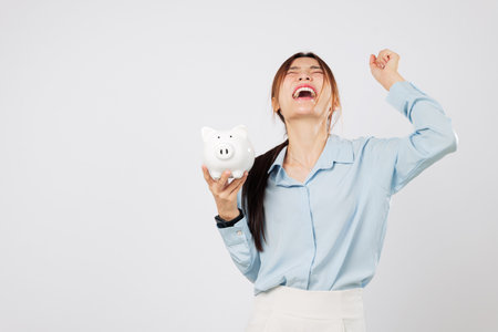 Piggy save money plan with happy woman with a fist up holding piggy bank excited to win in finance, showing success from smart saving and investment. isolated studio white backgroundの写真素材
