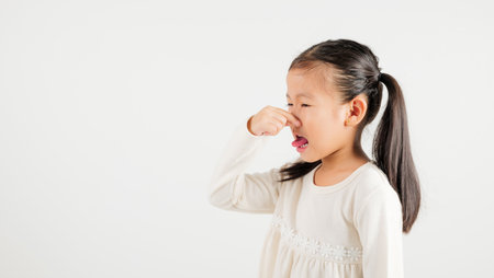 Asian young child unhappy what smell disgust expression squeezing nose with fingers. Kid girl kindergarten have something stinks bad smell situation, studio shot isolated on white backgroundの写真素材