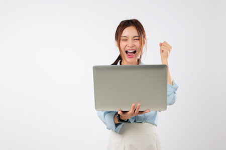 Laptop in front of happy young Asian woman excited cheering with smile, another laptop computer portable as she wins online with confidence and pride. isolated studio white backgroundの写真素材