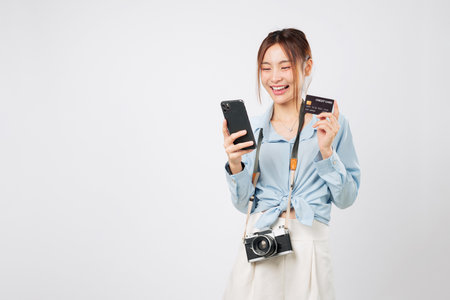 Travel app and travel photo camera held by Traveler tourist Asian woman using phone. She smiles holding credit card bank and mobile while shopping online during vacation. isolated white backgroundの写真素材