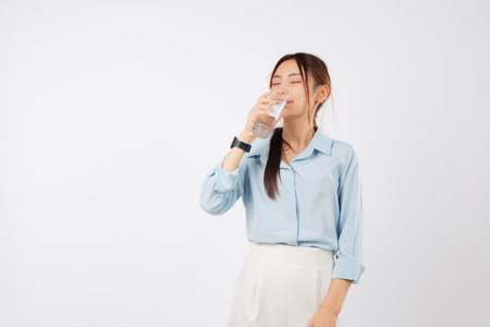 Woman glass drink liquid, young Asian hold a water glass. A refreshing face portrait of woman drinking clear water, showing health with fresh water intake, isolated studio white backgroundの写真素材