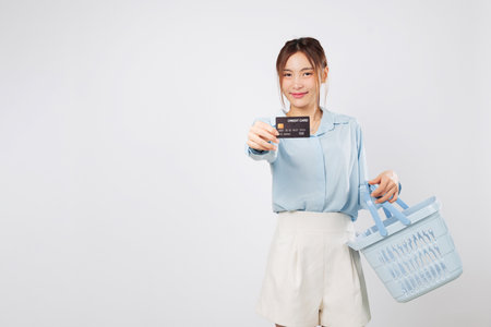 Shopping time with basket and credit bank card, Excited cheerful woman shopping wisely at supermarket with money and finance awareness. isolated studio white backgroundの写真素材