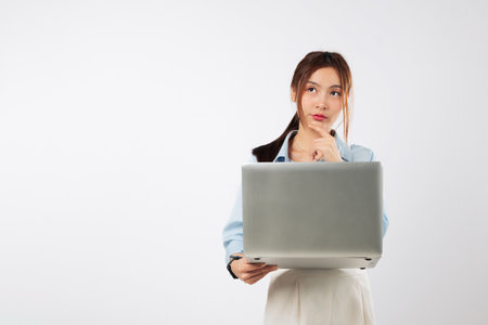 Laptop held tight as young Asian woman finger on chin with idea, another laptop computer portable represents smart thinking in modern workspace. isolated studio white backgroundの写真素材