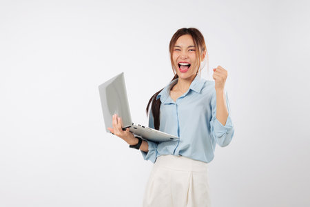 Laptop screen lights up as young Asian woman excited cheers for win, second laptop nearby represents her hard-earned success and happiness. isolated studio white backgroundの写真素材