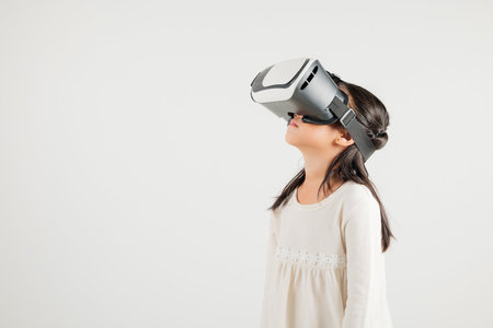 Smiling young kid girl confidence excited wear VR headset device during virtual reality experience isolated white background, Asian happy portrait kindergarten child playing video game studio shotの写真素材