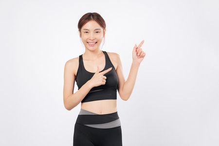 Point to the sky with a confident smile fit woman shows her points again, standing strong in black sportswear and embracing her fitness journey with grace and energy. isolated studio white backgroundの写真素材