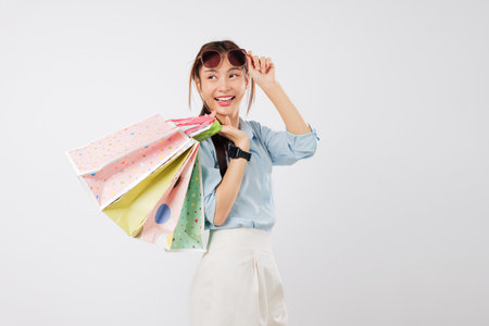 Happy asian woman excited posing with shopping bag and sunglasses, Take off sunglasses, cheerful young lady holds a beautiful shopping bag, isolated studio white backgroundの写真素材