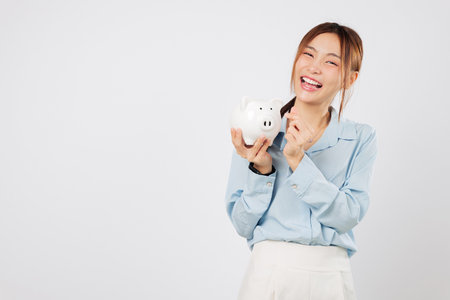Holding piggy and pointing finger to piggy bank excited woman saving money feeling happy with her progress and future secure through good banking. isolated studio white backgroundの写真素材