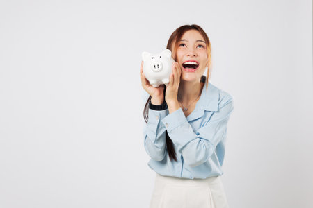 Hugging piggy bank with happy smile, excited Asian woman showing piggy money dream and celebrating success in saving habits and trusted banking services. isolated studio white backgroundの写真素材
