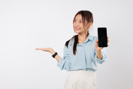 Portrait excited Asian woman hand holds a phone, showing its blank display screen with her palm up side. She is happy to present her new phone. isolated studio white backgroundの写真素材