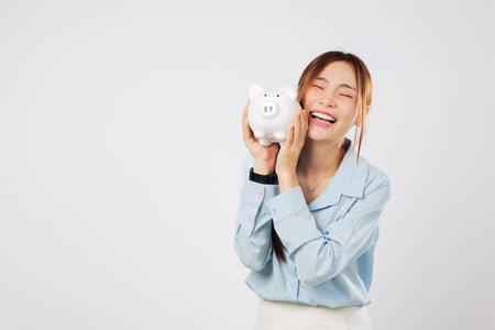 Hugging piggy bank with happy smile, excited Asian woman saving money piggy dream success through strong banking habits and personal financial growth. isolated studio white backgroundの写真素材