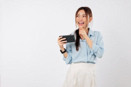 Excited young Asian woman smiles, holding a smart mobile phone and beginning to think. She has a serious question that makes her think intently. isolated studio white backgroundの写真素材