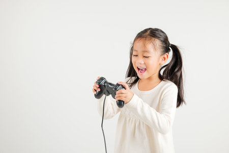 Asian happy portrait young kid girl smile lifestyle games technology holding joystick game playing on hands studio shot isolated white background with copy space, kindergarten child relaxation timeの写真素材