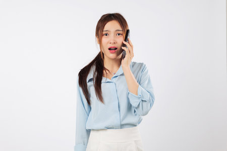 Asian young woman with phone shows surprise expression after a shock cellphone talk, experiencing another shock with sad and unhappy news, isolated studio white backgroundの写真素材
