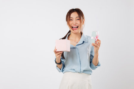Gift box opened with bright big smile by Asian woman celebrating special day, enjoying the excitement of receiving another thoughtful pink gift from someone she loves. isolated studio white backgroundの写真素材