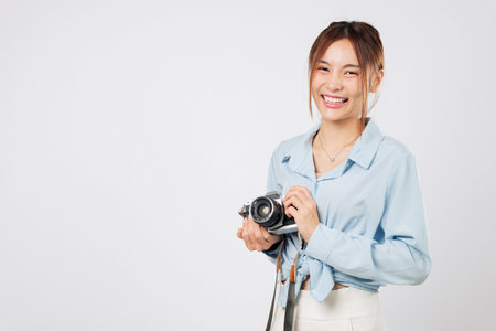 Tourist holding photo camera smiles brightly, classic tourist enjoying trip. Asian Young woman on traveler vacation captures happy moments during a peaceful holiday. isolated studio white backgroundの写真素材