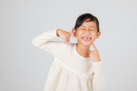 A cheerful girl points at her tooth gap proudly. The dentist highlights the importance of proper care during tooth loss and the changes in a child tooth gap. isolated white backgroundの写真素材